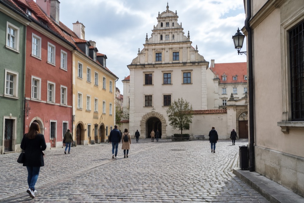Visitors walking a cobbled square between coloured merchant houses on a mild afternoon