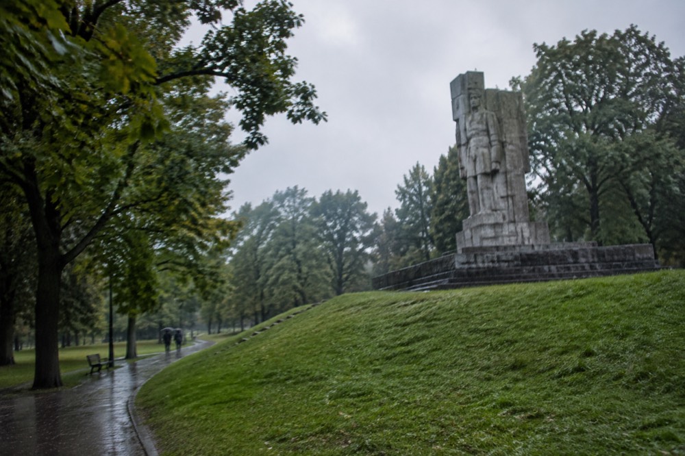 A stone military monument standing on a grassy hill with trees behind it