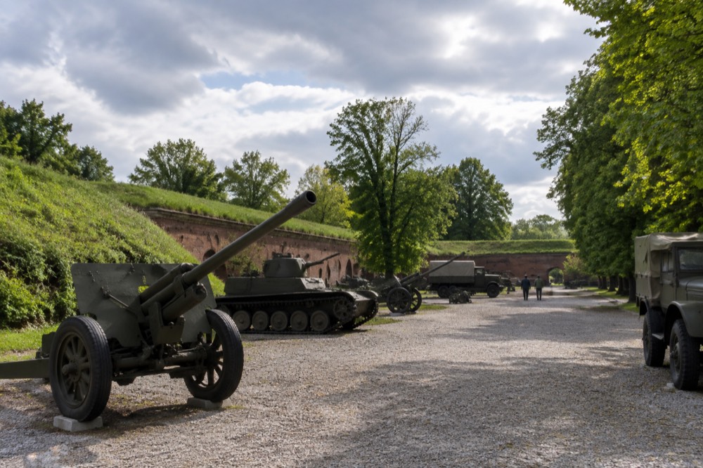 An outdoor display of military vehicles and cannons arranged on gravel in a park