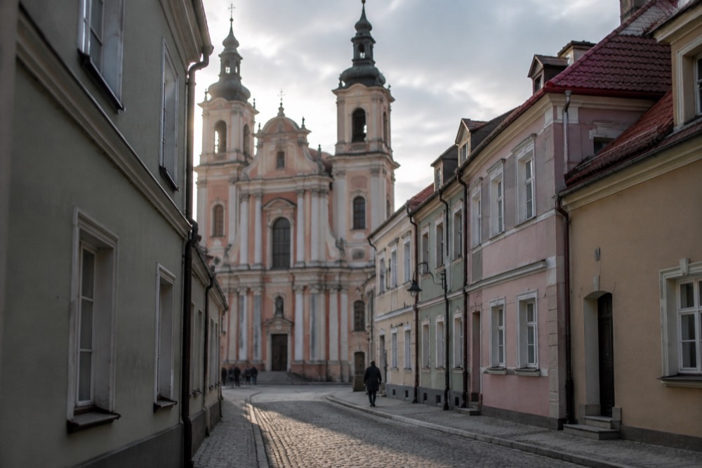 Cobblestone street corner with a church tower rising above pastel townhouses