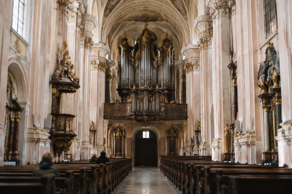 Church organ pipes above a dark carved case inside a baroque nave