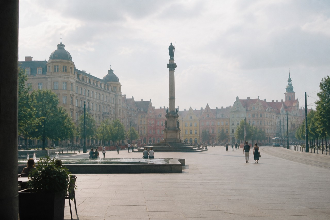 A wide city square in Poznan with a tall column monument at its centre and colourful historic buildings around the edge