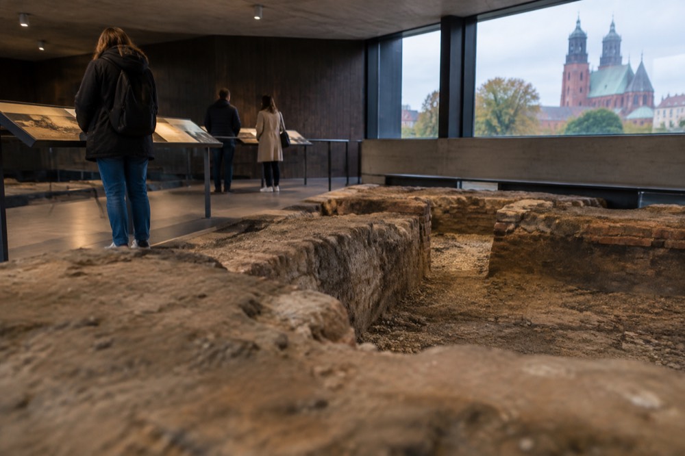 Visitors reading interpretive panels beside an excavated trench inside a museum hall