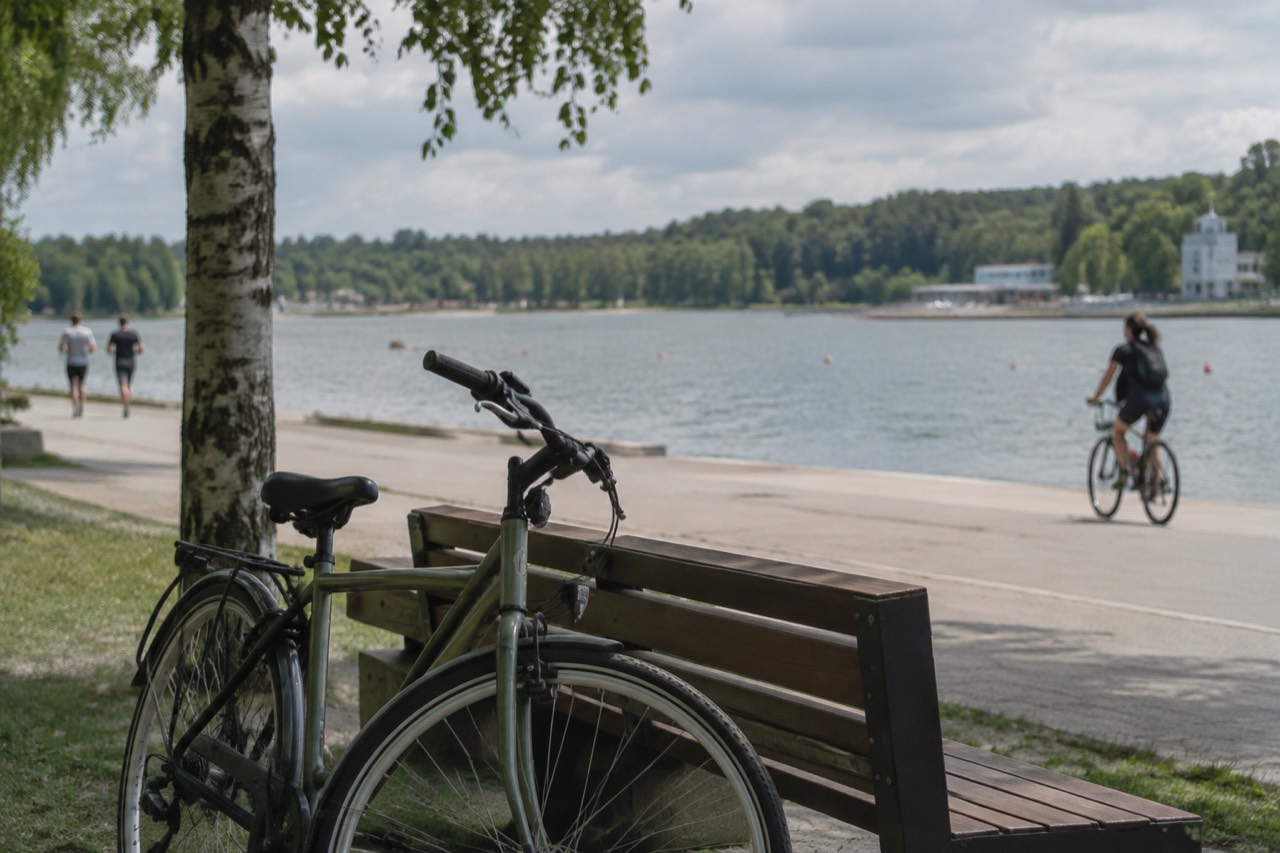 A wide recreational lake with a paved promenade, trees and buildings along the far shore