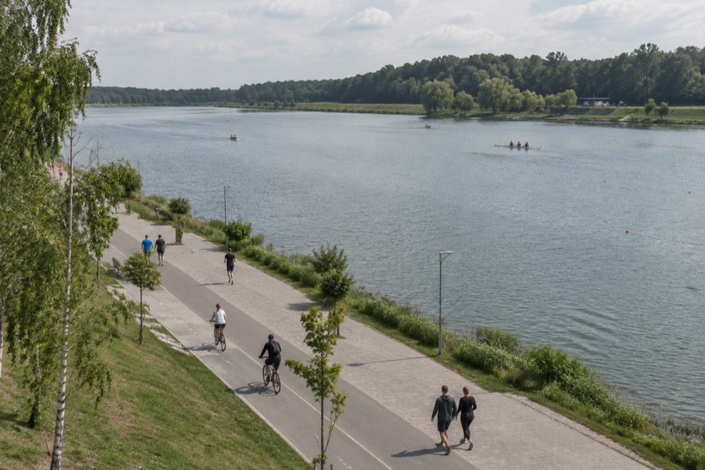 People walking and cycling along a waterfront path beside the lake on a sunny day