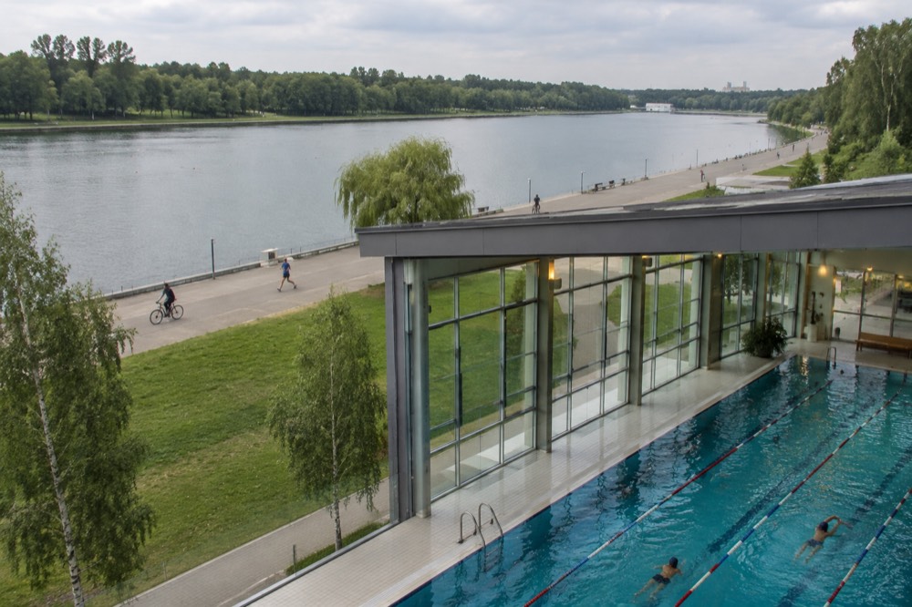 Swimmers in a large indoor pool with tall windows and warm lighting