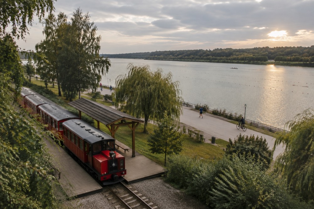 A small red narrow gauge train at a wooden station platform surrounded by trees