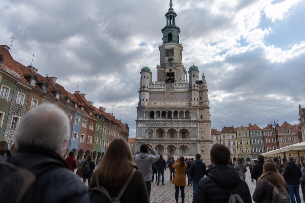 Crowd looking up at the Town Hall facade clock where two metal goats appear at noon in Poznan