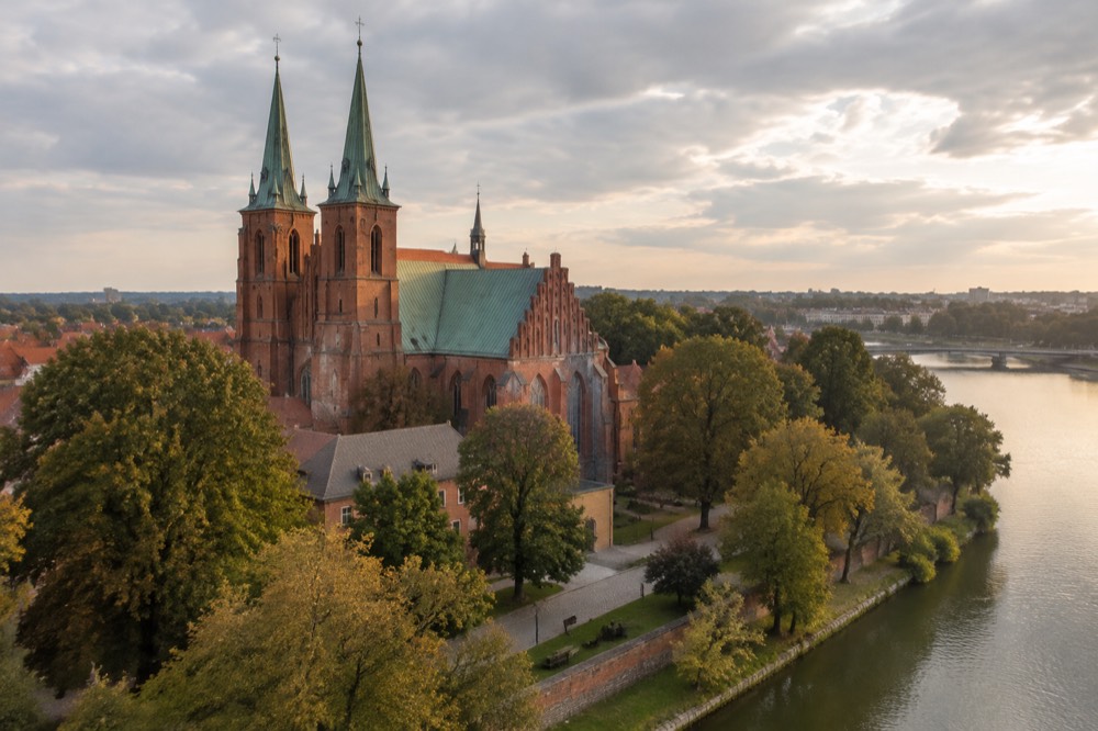 Red brick walls and tall arched windows of Poznan Cathedral seen from the island greenery