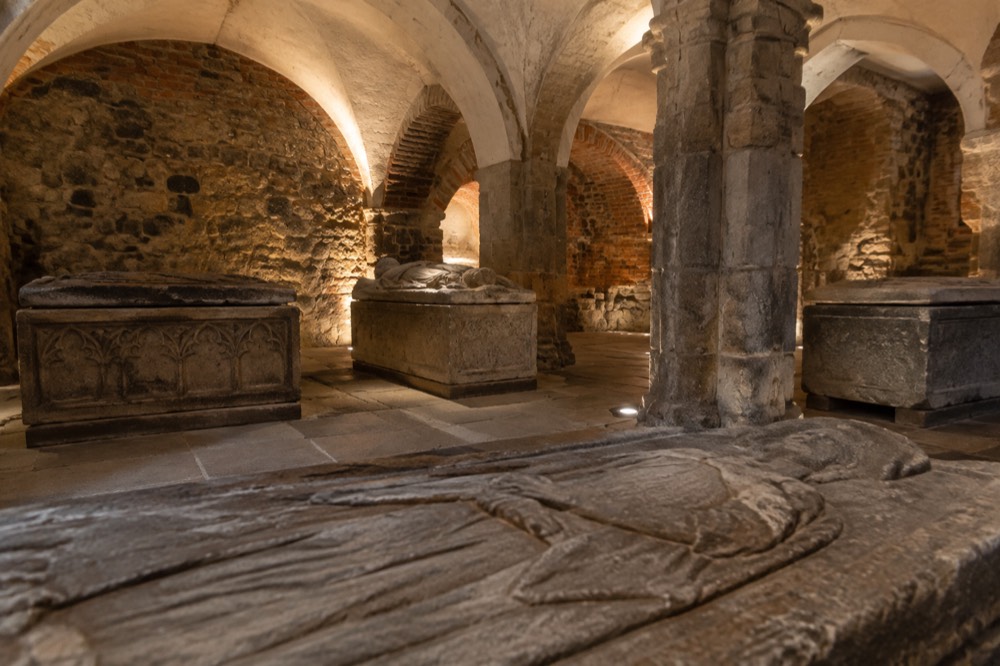 Stone crypt interior with old tombs lit by warm spotlights under Poznan Cathedral