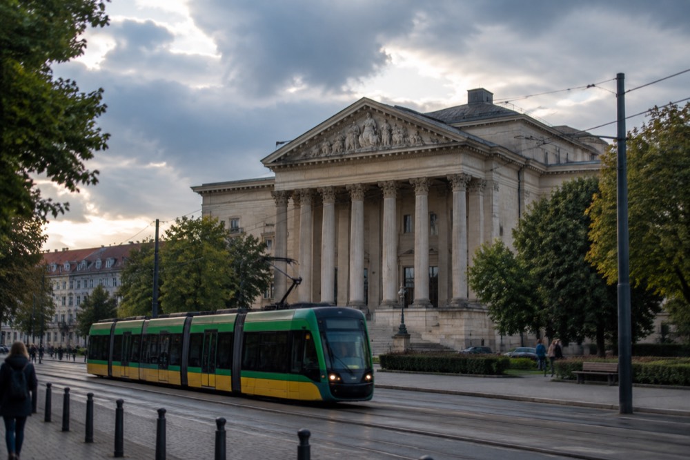 A modern Poznan tram moving along a city street in the early evening