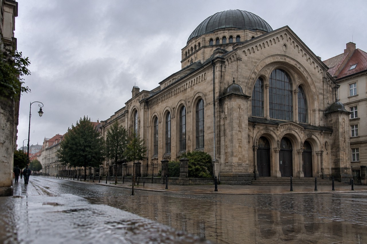 A historic synagogue building with a tall arched facade standing on a quiet street in Poznan