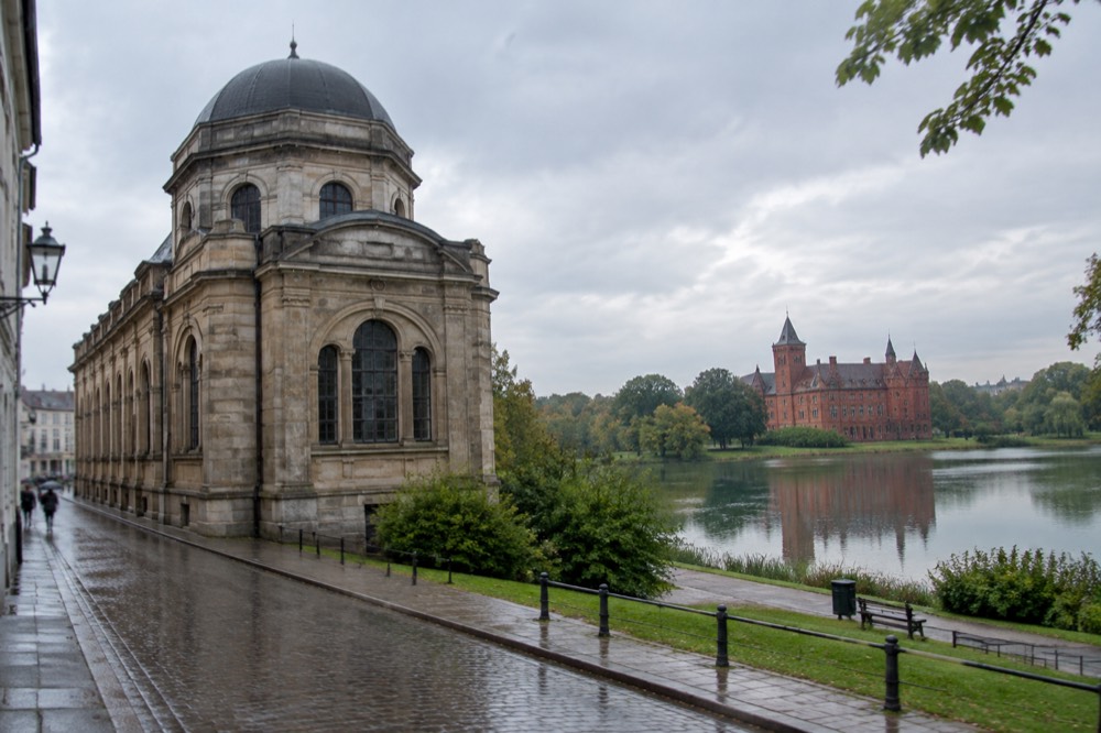 A red brick castle reflected in a lake surrounded by parkland near Poznan