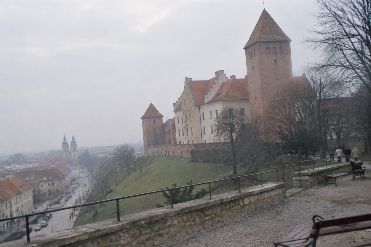 A reconstructed castle with brick towers standing on a green hill above a city street