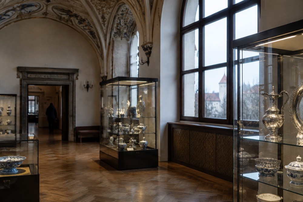 An ornate gallery interior with glass display cases of silver and ceramics