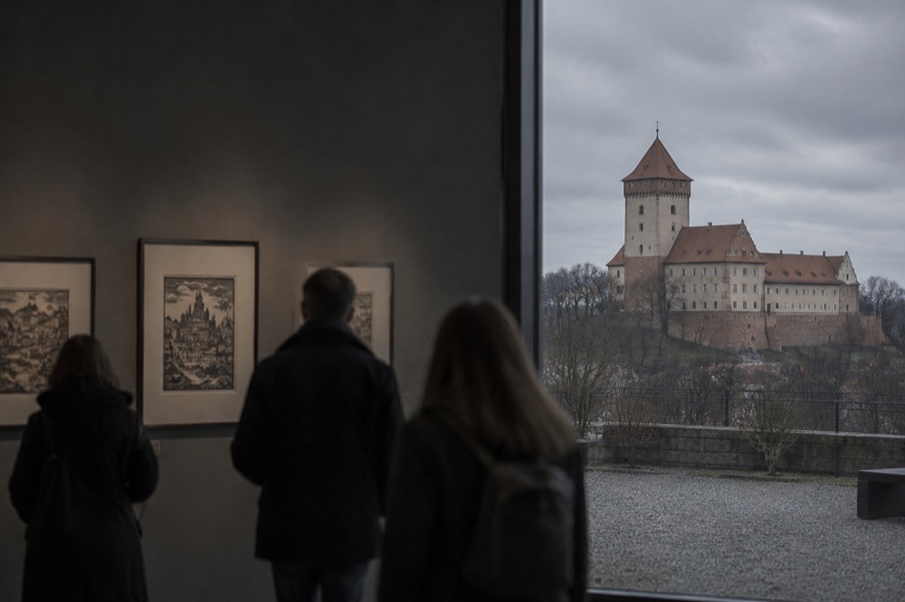 Visitors looking at framed woodblock prints in a dim museum gallery