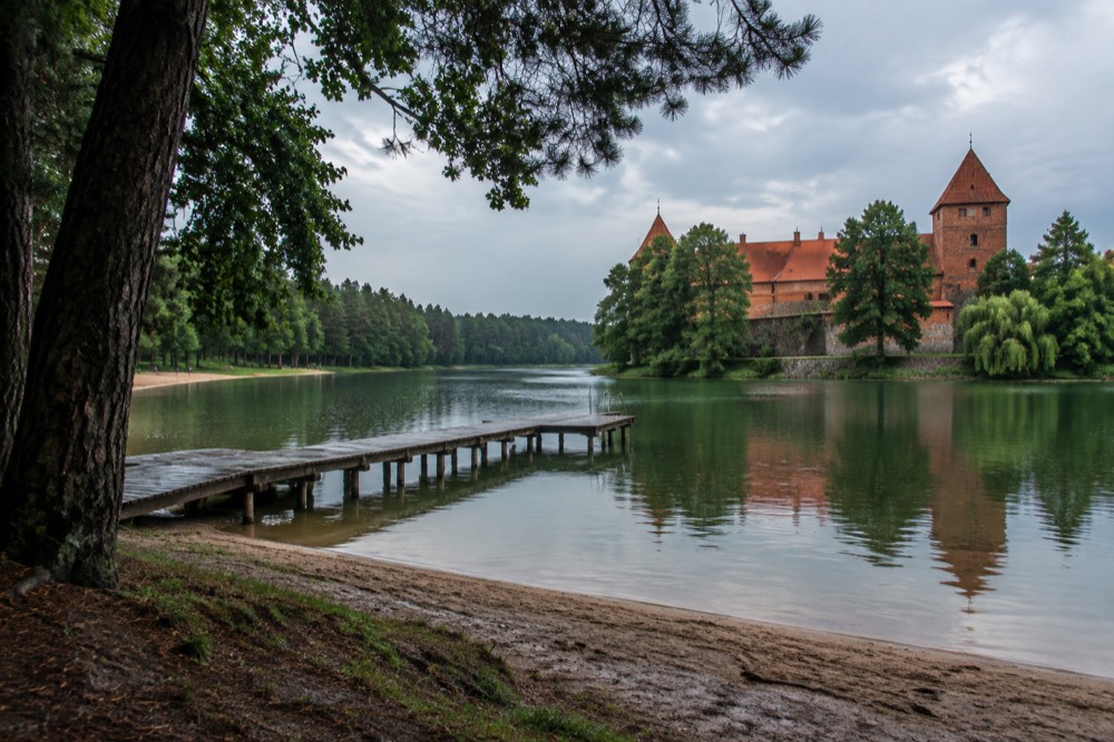 A red-brick castle reflected in a moat surrounded by old trees