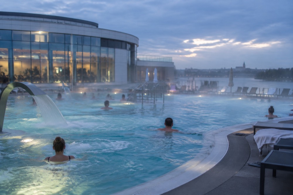Turquoise thermal pool with massage jets and swimmers relaxing in warm water