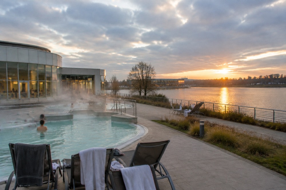 Sunset over a lake with a promenade and distant pool building glowing warmly