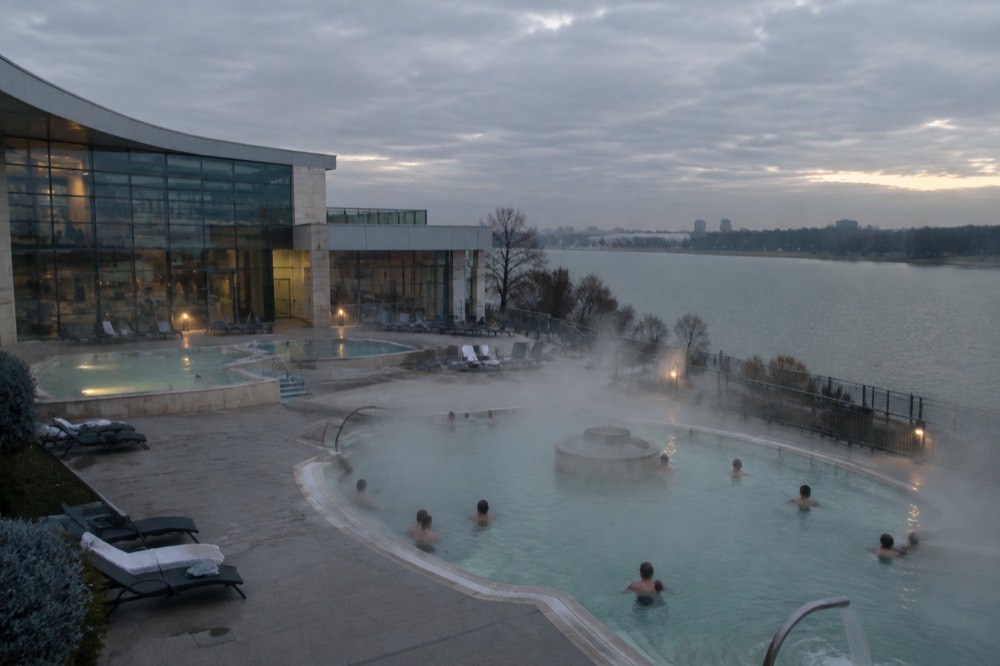 Steam rising from an outdoor thermal pool at dusk with bathers in the warm water