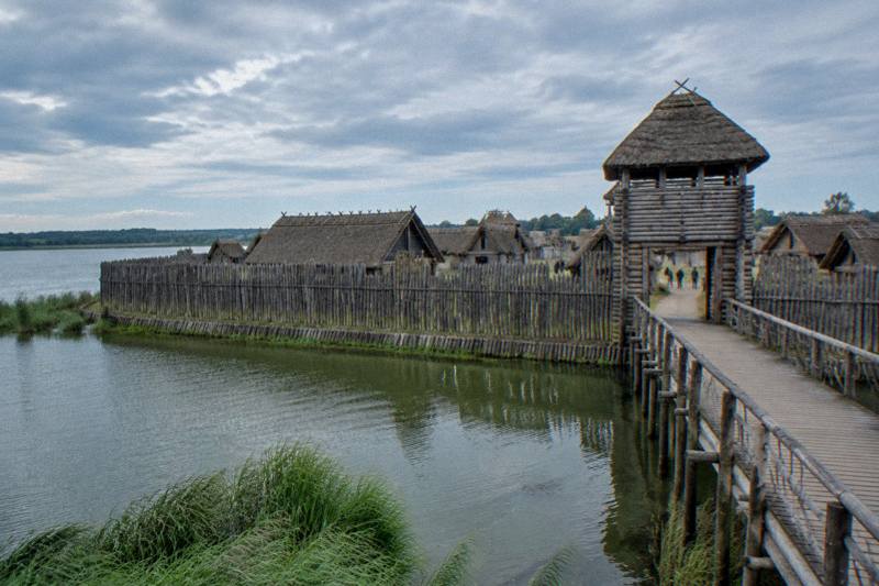 The timber palisade and thatched log houses of the reconstructed Iron Age settlement at Biskupin beside a lake