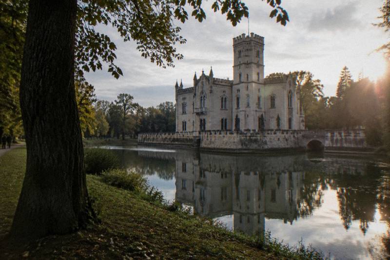 The pale neo-Gothic Kornik Castle with battlements and a moat among old trees